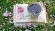 an open book with a cup of coffee on top of it next to pink flowers