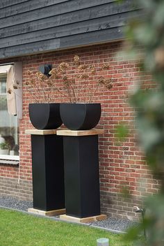 two large black vases sitting on top of each other in front of a brick building