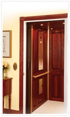 an open wooden door in a room with white carpeting and yellow walls, next to a table with flowers on it