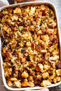 a casserole dish filled with stuffing and topped with a spoon in someone's hand