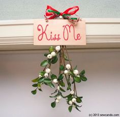 a wooden sign that says kiss me hanging from a window sill with white berries and green leaves