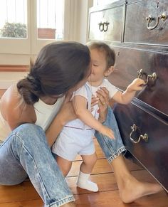 a woman holding a baby in her lap and kissing it's face next to a dresser