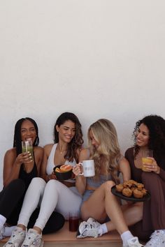 four women sitting on a bench with drinks and food