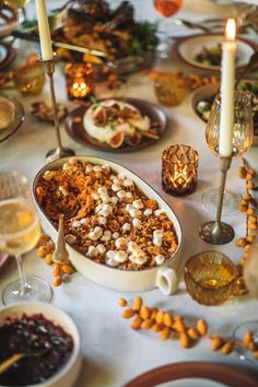 a table topped with plates and bowls filled with food next to candlelight candles on top of a white table cloth