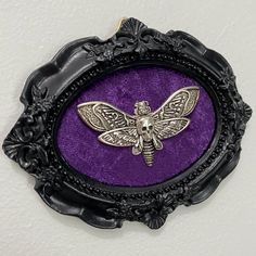 a bee brooch sitting on top of a purple velvet covered button in a black frame