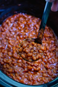 the spoon is full of baked beans in the slow cooker