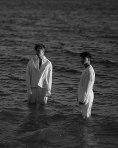 two men standing in the water near each other, one wearing a white shirt and tie