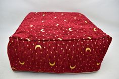 a red and yellow ottoman cover with gold stars and crescents on the top, sitting on a white surface