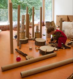 a young boy is playing with wood in an art room filled with trees and logs