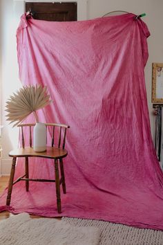 a pink blanket draped over a chair in front of a table with a vase on it