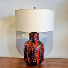 a red and black vase sitting on top of a wooden table next to a lamp