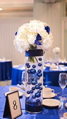 a vase filled with white flowers sitting on top of a blue table cloth covered table