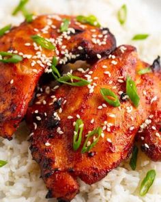 two pieces of chicken with sesame seeds on top of white rice and garnished with green leaves