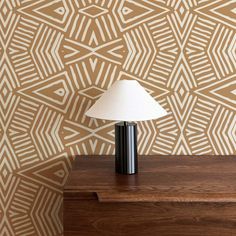 a lamp sitting on top of a wooden table next to a wallpapered wall