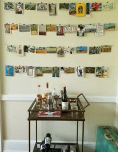 a bar cart in front of a wall with pictures on it and wine bottles sitting on top