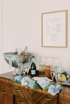 a table topped with lots of wine glasses and bottles on top of a wooden dresser