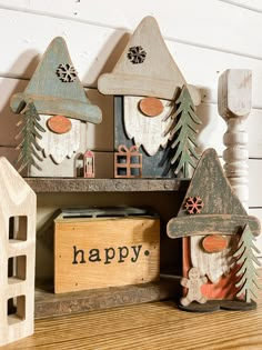 three wooden gnome houses with happy written on the front and bottom, sitting next to each other