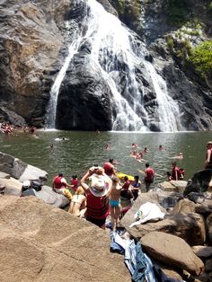 many people are swimming in the water near a waterfall and some rocks with towels on them