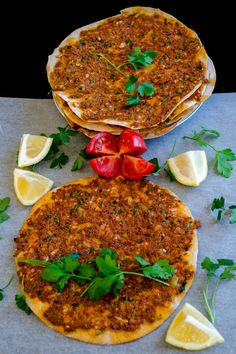 two pita breads with tomatoes and herbs on top, next to lemon wedges