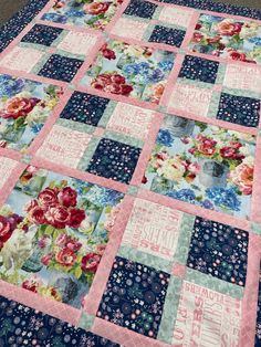 a blue and pink patchwork quilt with flowers on the front, along with words written in large letters