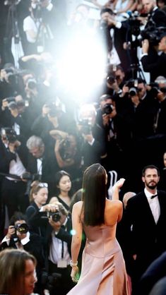 the back of a woman's dress as she walks down a red carpet in front of photographers