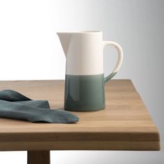 a white and green pitcher sitting on top of a wooden table next to a tea towel