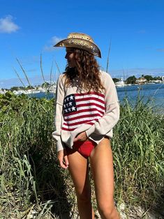 a woman in a patriotic sweater and hat is standing on the sand by the water