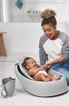 a woman is playing with a baby in a bathtub that's on the floor