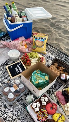 a table topped with lots of food on top of a beach next to the ocean