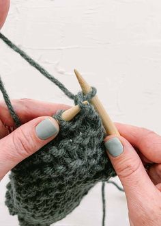 two hands holding a knitting needle over a green crochet bag with yarn on it