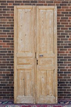 an old wooden double door in front of a brick wall with a rug on the floor