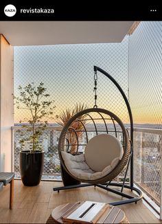 a hanging egg chair on a balcony overlooking the ocean at sunset or dawn with an open book and potted plant in the foreground