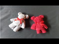 two crocheted teddy bears sitting next to each other on a gray surface with red ribbon