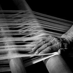 an old woman's hands weaving on a loom with long white yarn in black and white