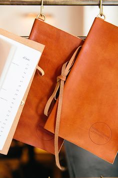 two brown leather notebooks are hanging on a rack with a notepad and pen