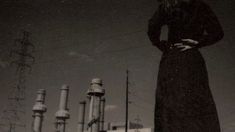 a woman in a long black dress standing next to some power lines and poles with her hands on her hips