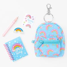 a blue backpack with rainbows and stars on it next to a notepad, pencil holder, and keychain