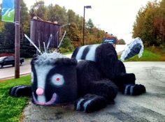 a large black and white cow laying on the side of a road next to a lush green field