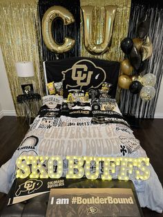 the bed is decorated with black and gold balloons, foil streamers, and an i am boulder sign