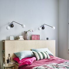 a bed with pink and green pillows on top of it next to two wall lights