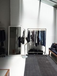 an empty room with clothes hanging on racks and a bench in front of the window