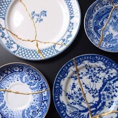 four blue and white plates with twig stems sticking out of the top, on a black surface