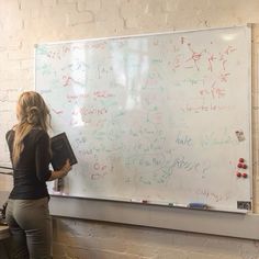 a woman standing in front of a whiteboard with writing on it and holding a book