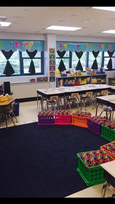 an empty classroom filled with lots of desks and colorful boxes on the floor in front of windows