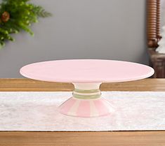 a pink cake plate sitting on top of a table next to a potted plant