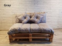 a couch made out of wooden pallets with pillows on top and bottom, sitting in front of a brick wall