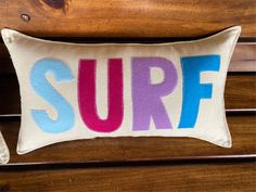 a pillow with the word surf painted on it sitting on top of a wooden bench