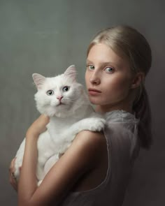 a woman is holding a white cat in her arms and looking at the camera with an intense look on her face