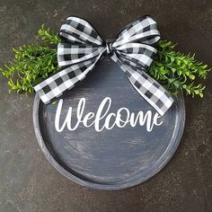 a welcome sign with a bow hanging on the front of it and greenery around it