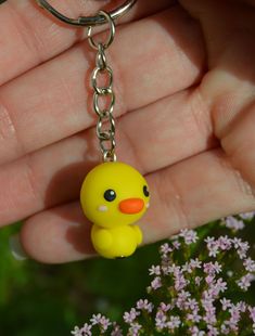 a yellow rubber ducky keychain hanging from a silver metal chain with flowers in the background